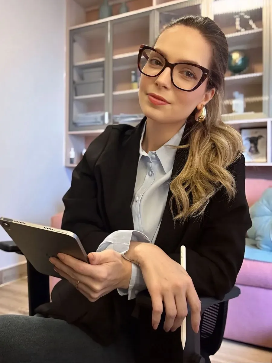 Dra. Amanda Arnoni sentada, segurando um tablet e uma caneta, olhando para a câmera