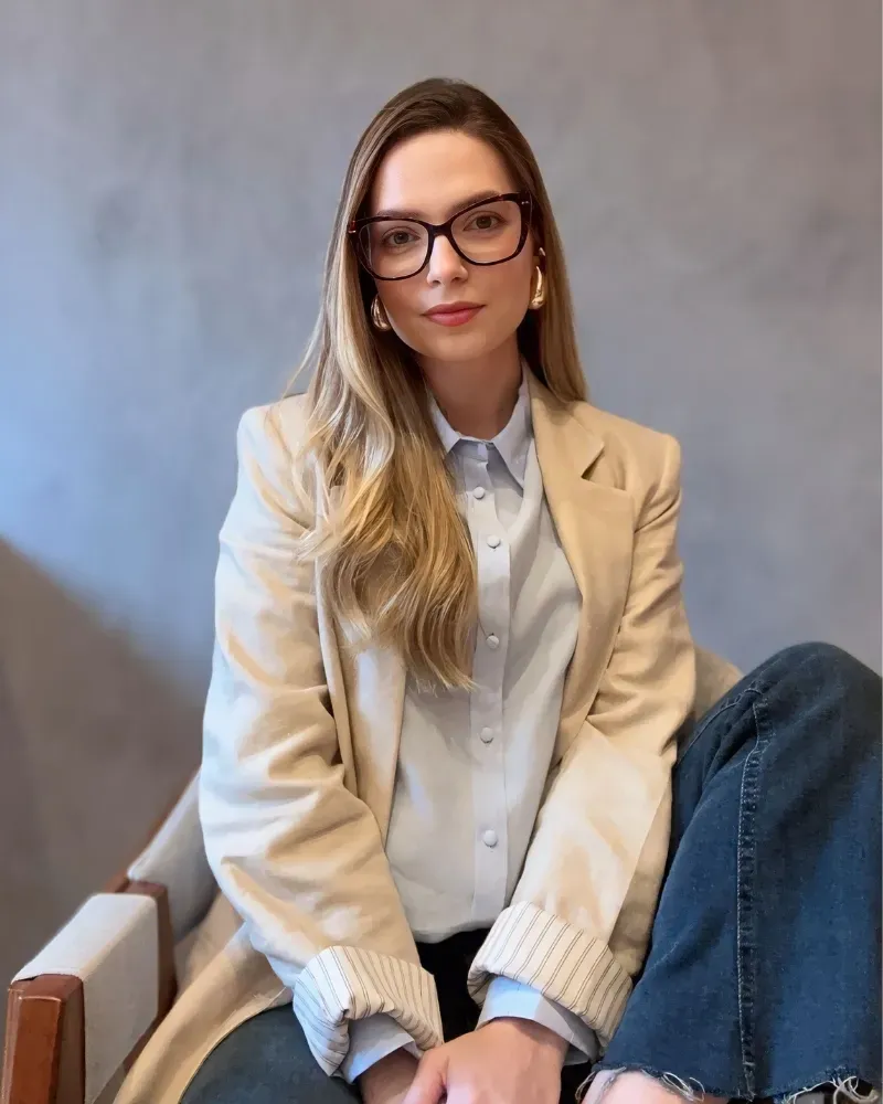 Retrato da Dra. Amanda Arnoni, de blazer bege e camisa azul-clara, olhando para a câmera